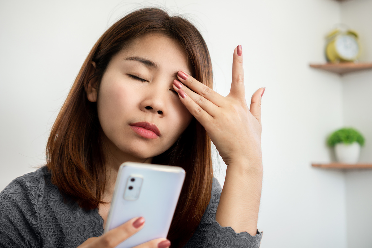 Asian woman suffering from eye pain from phone screen time cause